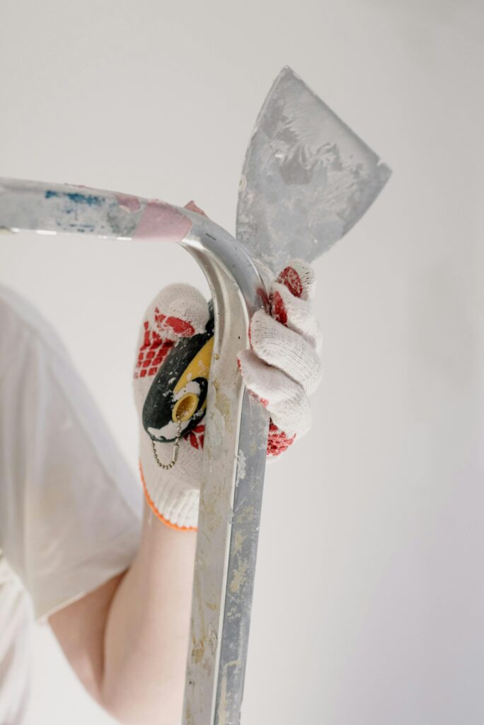 Crop anonymous male in gloves holding trowel while standing on ladder during renovation